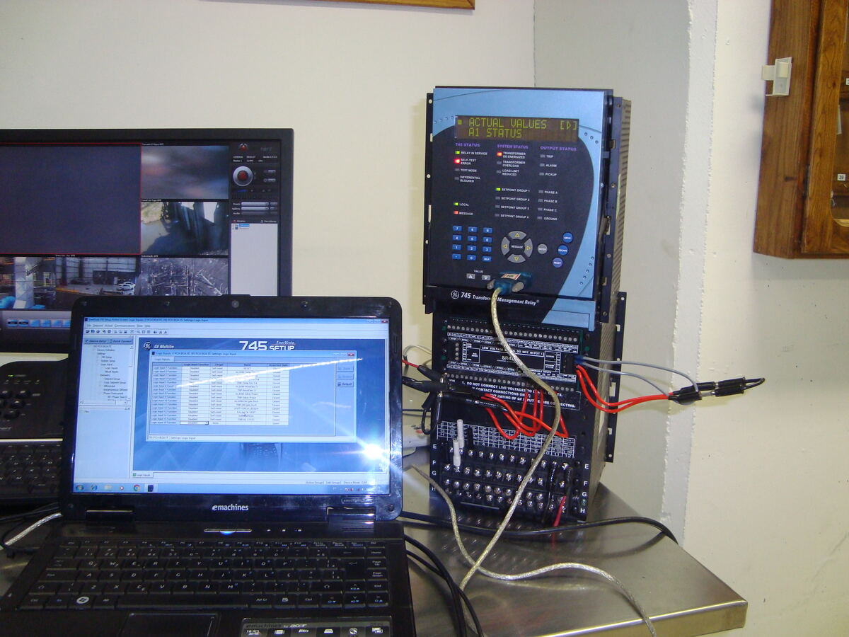 Relé de proteção GE 745 instalado em painel, com notebook rodando o software de configuração